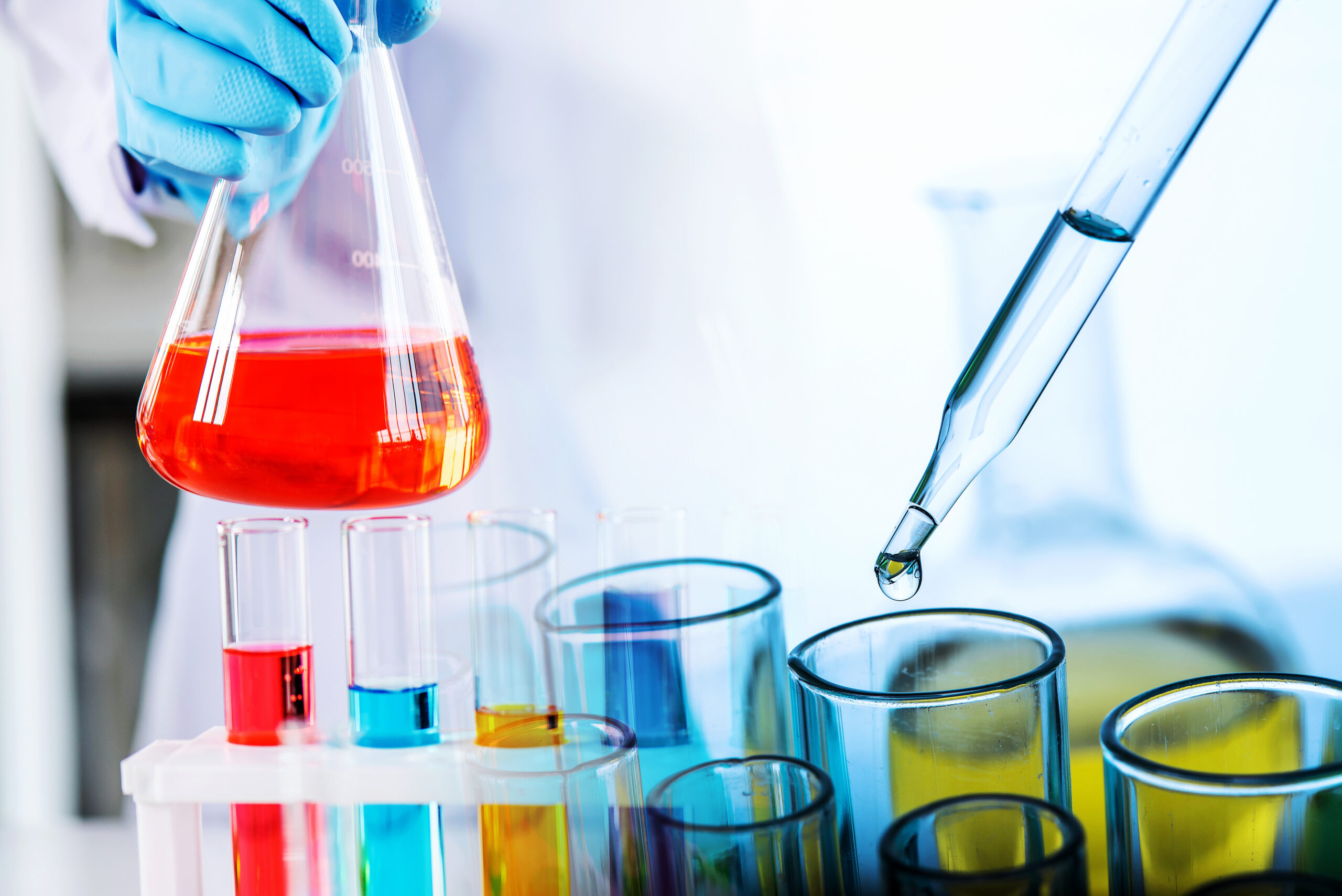 hand of scientist holding flask with lab glassware and test tubes in chemical laboratory background, science laboratory research and development concept